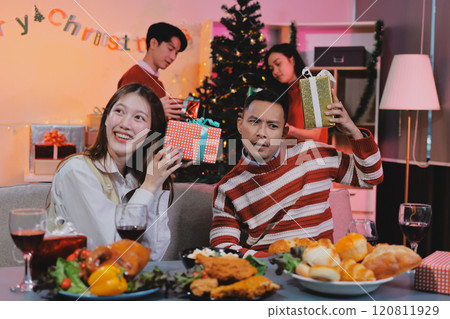 Friends opening Christmas gifts in living room 120811929