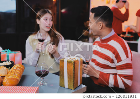 Group of happy Asian friends celebrating Christmas and decorate the Christmas tree indoors. Beauty woman with Christmas Gifts. New Year party. Woman hands decorate Christmas tree red ball, bauble. 120811931