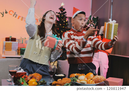 Group of happy Asian friends celebrating Christmas and decorate the Christmas tree indoors. Beauty woman with Christmas Gifts. New Year party. Woman hands decorate Christmas tree red ball, bauble. 120811947