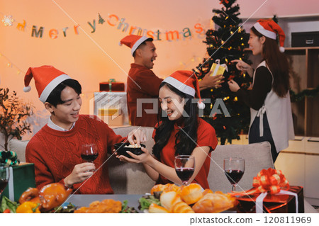 Group of young Asian man and women as friends having fun at a New Year's celebration, holding gift boxes standing by Christmas tree decoration, midnight countdown Party at home with holiday season. Group of young Asian man and women as friends having fun at a New Year's celebration, holding gift boxes standing by Christmas tree decoration, midnight countdown Party at home with holiday season. 120811969