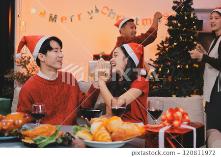 Group of young Asian man and women as friends having fun at a New Year's celebration, holding gift boxes standing by Christmas tree decoration, midnight countdown Party at home with holiday season. Group of young Asian man and women as friends having fun at a New Year's celebration, holding gift boxes standing by Christmas tree decoration, midnight countdown Party at home with holiday season. 120811972