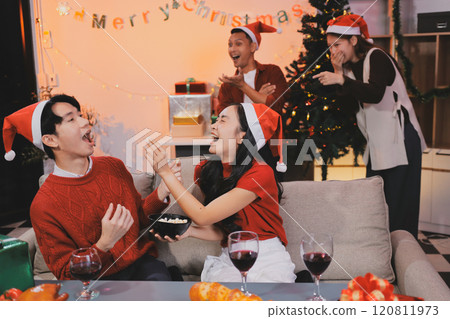 Group of young Asian man and women as friends having fun at a New Year's celebration, holding gift boxes standing by Christmas tree decoration, midnight countdown Party at home with holiday season. 120811973