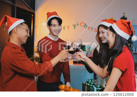 Group of young Asian man and women as friends having fun at a New Year's celebration, holding gift boxes standing by Christmas tree decoration, midnight countdown Party at home with holiday season. 120812008