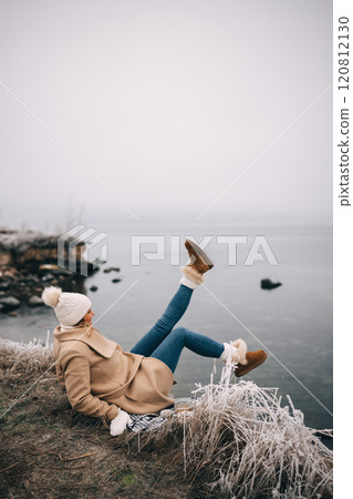 Young happy woman sitting by the sea raised leg up 120812130