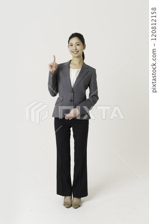 Full-body portrait of a young woman in a suit pointing at something on a white background, vertical position 120812158