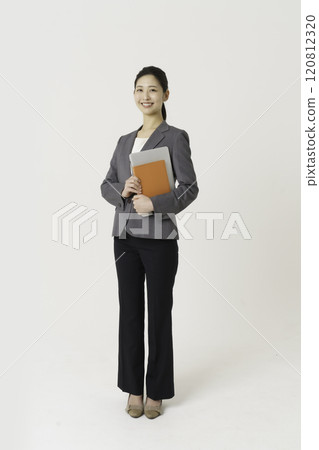 Full-body portrait of a young woman wearing a suit standing with a laptop and notebook against a white background, vertical position Full-body portrait of a young woman wearing a suit standing with a laptop and notebook against a white background, vertical position 120812320