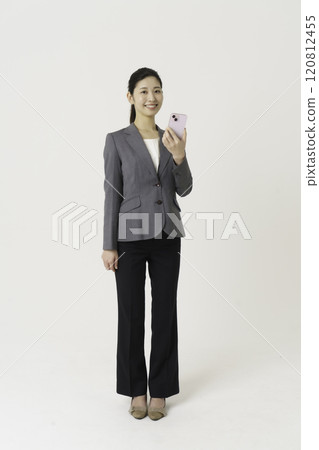 Full-body portrait of a young woman wearing a suit and standing with a smartphone against a white background, vertical position Full-body portrait of a young woman wearing a suit and standing with a smartphone against a white background, vertical position 120812455