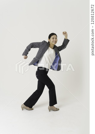 Full-body portrait of a young woman jumping in a suit against a white background, vertical position 120812672