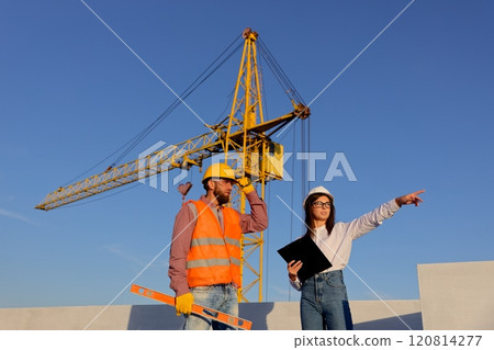 Construction manager and engineer discussing building project on site with crane in background 120814277