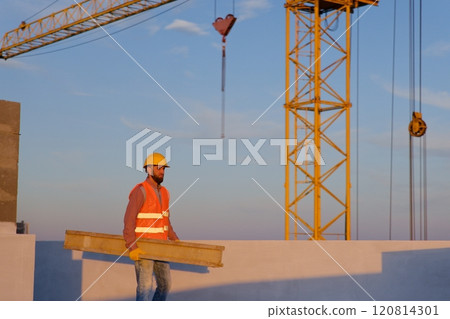 Construction worker carrying wooden plank on rooftop at sunset Construction worker carrying wooden plank on rooftop at sunset 120814301