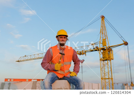 Construction worker sitting and holding hammer at construction site 120814304