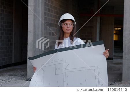 Female architect holding blueprint, inspecting construction site progress 120814340