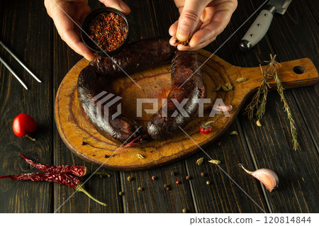 A skilled chef prepares a delectable sausage by adding an array of spices on a rustic wooden cutting board, showcasing the love for culinary artistry and fresh ingredients 120814844