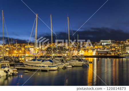 Panorama of the Norwegian city of Tromso on a winter evening during the Christmas season. The boat dock and downtown are illuminated by city lights. Panorama of the Norwegian city of Tromso on a winter evening during the Christmas season. The boat dock and downtown are illuminated by city lights. 120814873