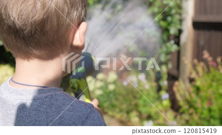Funny little boy watering lawn plants in garden housing backyard. Adorable child playing with irrigation hose at hot sunny summer outdoors. Children help with housework. activity for kids. Childhood Funny little boy watering lawn plants in garden housing backyard. Adorable child playing with irrigation hose at hot sunny summer outdoors. Children help with housework. activity for kids. Childhood 120815419