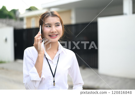 Pretty asian office worker having pleasant phone conversation while standing outdoor 120816848