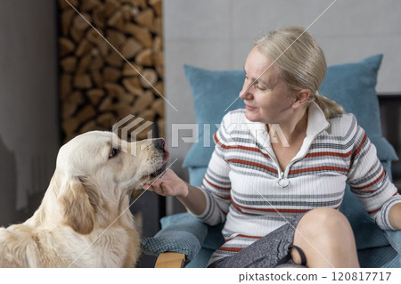 A smiling woman interacting with a Golden Retriever indoors, showcasing warmth, affection, and a cozy domestic atmosphere. A smiling woman interacting with a Golden Retriever indoors, showcasing warmth, affection, and a cozy domestic atmosphere. 120817717