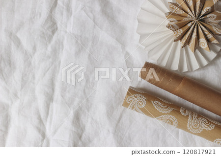 Christmas festive composition. Neutral gift wrapping paper and decorative paper stars, rosette on white linen table cloth background. Gift wrapping, crafting concept. Winter composition. Flat lay, top 120817921