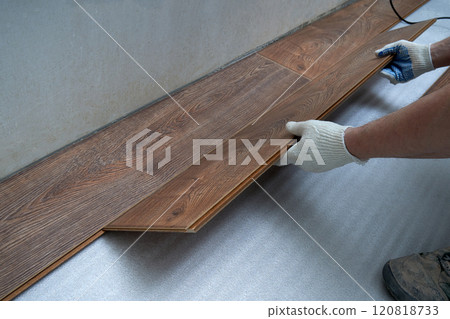 Hands skillfully place wooden panels on a smooth surface, showcasing the intricate design. Sunlight gently illuminates the contemporary room, enhancing the ambiance of the renovation. 120818733