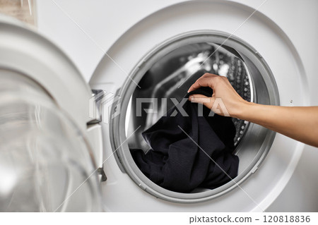 Woman putting black cotton clothes into the washing machine, close-up 120818836
