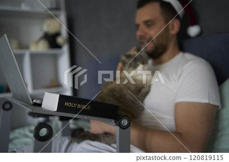 A 30-year-old man with a Bible attends an online church service, talks with the pastor 120819115