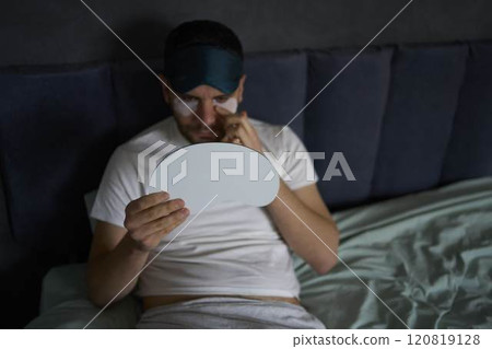 a 30-year-old man with a silk mask for sleep applying patches under the eyes from swelling, wrinkles, a 30-year-old man with a silk mask for sleep applying patches under the eyes from swelling, wrinkles, 120819128