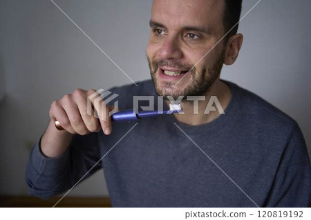 A 30-year-old man brushes his teeth with charcoal toothpaste using an electric toothbrush 120819192