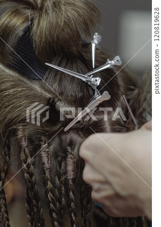 Process of braiding dreadlocks, close-up. Human hair, hairdressing clips and hairdressers fingers at work, vertical image, selective focus. 120819628