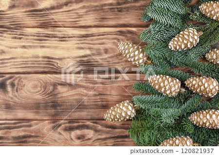 Christmas brown wooden background with green fir twigs and golden cones toys. Beautiful tree pattern. Place for congratulations, news, suggestions 120821937