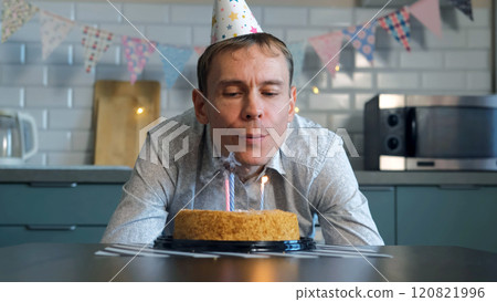 In a cozy kitchen, a disheartened man extinguishes birthday candles on a cake, reflecting on another solo celebration In a cozy kitchen, a disheartened man extinguishes birthday candles on a cake, reflecting on another solo celebration 120821996