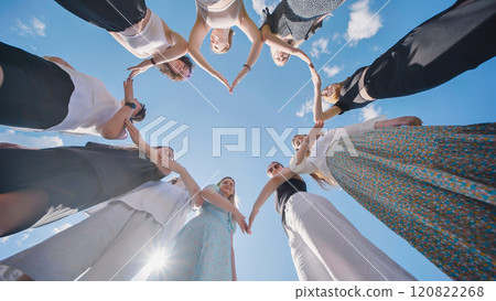 Group of friends joining hands forming heart shape against blue sky Group of friends joining hands forming heart shape against blue sky 120822268