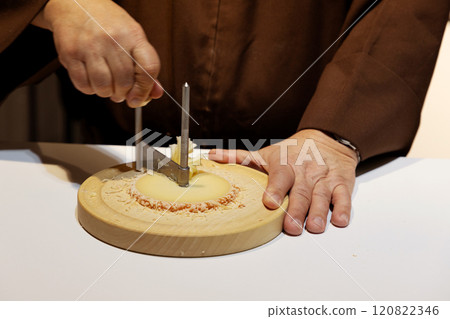 middle section of a middle aged man with hands in monk's robe cutting cheese 120822346