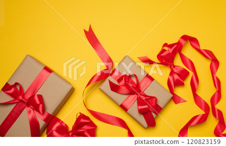Two boxes tied with red ribbon on yellow background, festive background. Two boxes tied with red ribbon on yellow background, festive background. 120823159