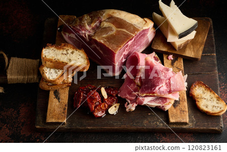 A piece of prosciutto, slices of ciabatta and cheese on a wooden board A piece of prosciutto, slices of ciabatta and cheese on a wooden board 120823161