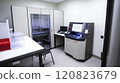 A modern genetic testing lab featuring advanced DNA sequencing machines, a workstation displaying genetic data on computers, and a centrifuge for sample preparation. The room has white walls 120823679