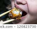 A detailed closeup view of a person relishing sushi with chopsticks 120823730