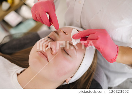 The beautician uses a hot pink glove to apply skincare treatment on the client, bringing a pop of color and uniqueness to the scene. The beautician uses a hot pink glove to apply skincare treatment on the client, bringing a pop of color and uniqueness to the scene. 120823992