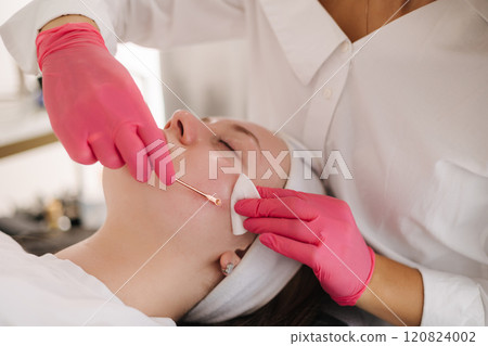The beautician uses a hot pink glove to apply skincare treatment on the client, bringing a pop of color and uniqueness to the scene. 120824002