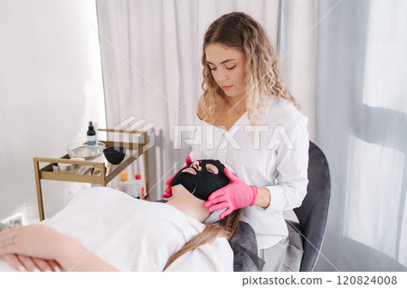 Aesthetician applies a hydrating mask to the face, deeply nourishing the skin and restoring its natural softness and elasticity 120824008