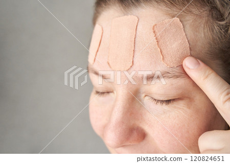 Female caucasian adult with bandages on forehead applying gentle pressure Female caucasian adult with bandages on forehead applying gentle pressure 120824651