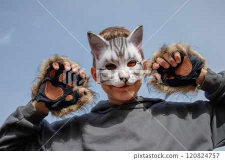 A playful child wearing a cat mask and furry gloves, posing with a cheerful expression against a clear blue sky. A playful child wearing a cat mask and furry gloves, posing with a cheerful expression against a clear blue sky. 120824757