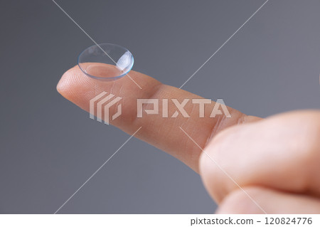 Vision correction and maintenance concept. Close-up of contact lens on finger on grey background. 120824776