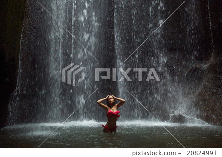 A young, slender woman in a pink swimsuit swims in an incredibly beautiful mystical waterfall in a cliff on the popular island of Bali. A young, slender woman in a pink swimsuit swims in an incredibly beautiful mystical waterfall in a cliff on the popular island of Bali. 120824991