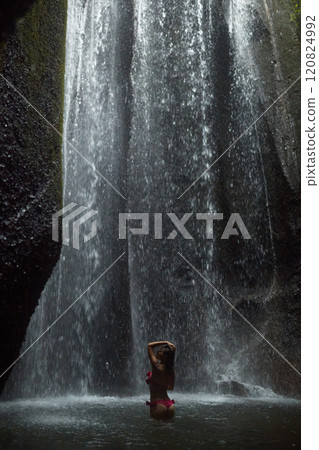 A young, slender woman in a pink swimsuit swims in an incredibly beautiful mystical waterfall in a cliff on the popular island of Bali. A young, slender woman in a pink swimsuit swims in an incredibly beautiful mystical waterfall in a cliff on the popular island of Bali. 120824992