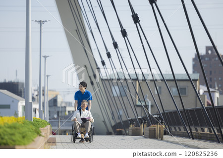Care staff pushing a wheelchair outdoors 120825236
