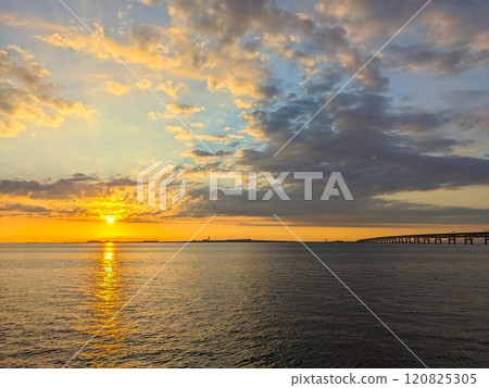 Rinku Town, Japan - 08.12.2024: Sunset at Osaka Bay with Kansai Internation Aiport at the horizon connected by a bridge at the golden hour under a blue and golden gradient sky and dramatic clouds 120825305
