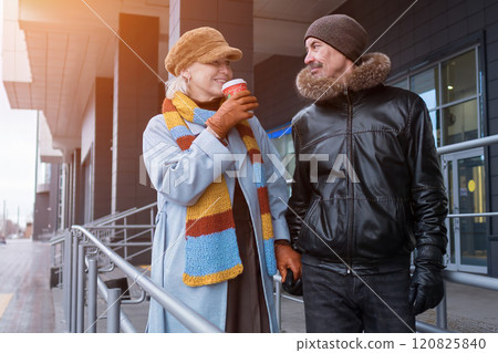 Happy senior couple walking and drinking coffee outdoors in winter 120825840