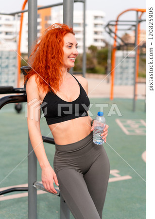Thoughtful happy sporty woman holding water bottle 120825906