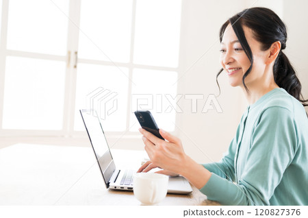 一名中年婦女單手拿著智慧型手機操作電腦 120827376