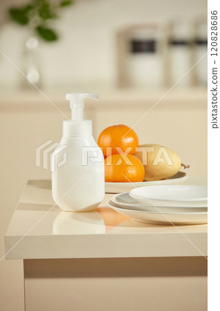Mockup for advertising of cleaning products in the context of the kitchen. A bottle without brand is placed in the corner of the kitchen island, besides some fresh fruits and white porcelain plates 120828686